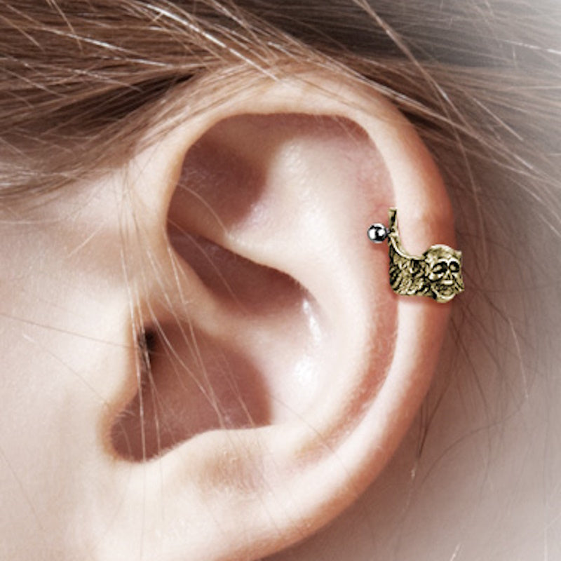 An antique gold skull helix earring cuff pictured on the ear of a model.