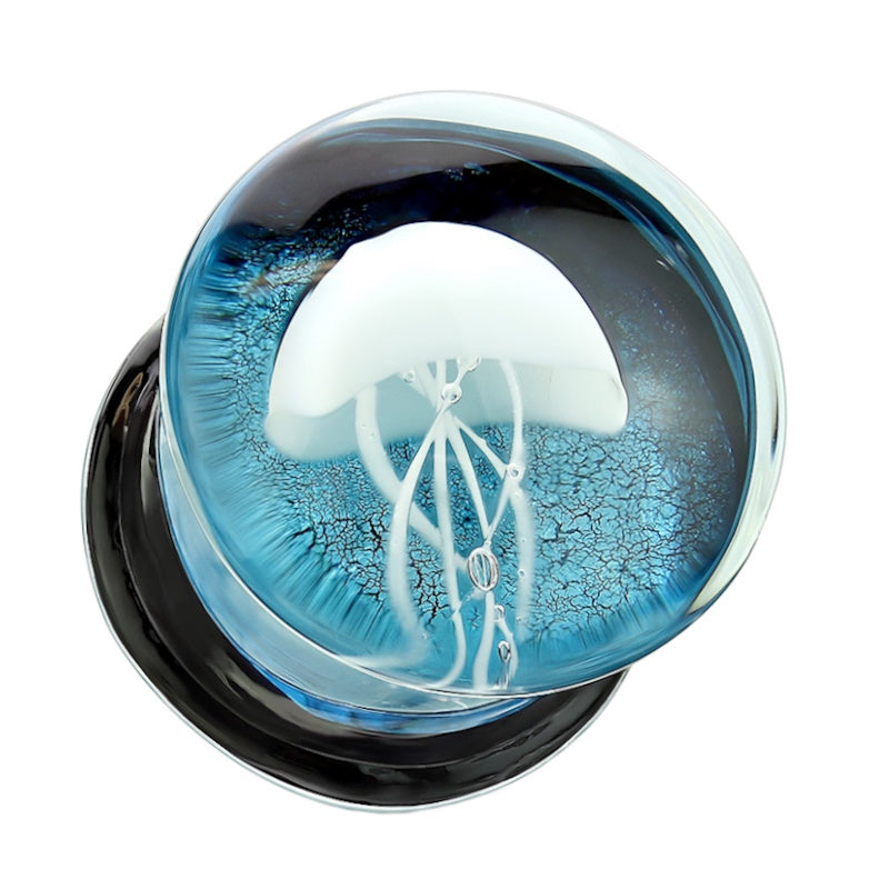 One of a pair of glass floating jellyfish gauges with a white jellyfish in front of a blue background with the ear gauge pictured against a white background.