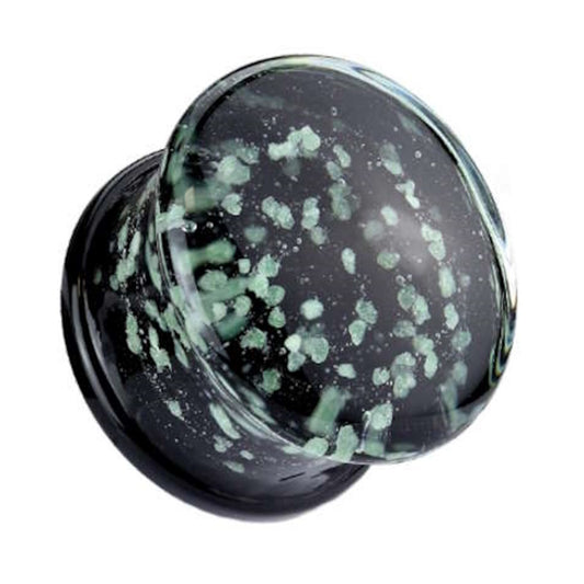 One of a pair of glass glow in the dark gauges with green glowing speckles embedded in the glass plug pictured against a white background.