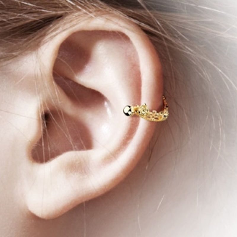 A gold plated crown earring cuff pictured on the ear of a model.