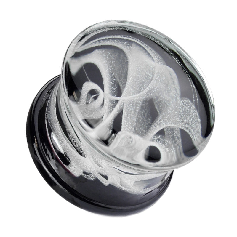 One of a pair of smoky glass ear plugs with a swirling smoke design embedded in the glass plugs pictured against a white background.