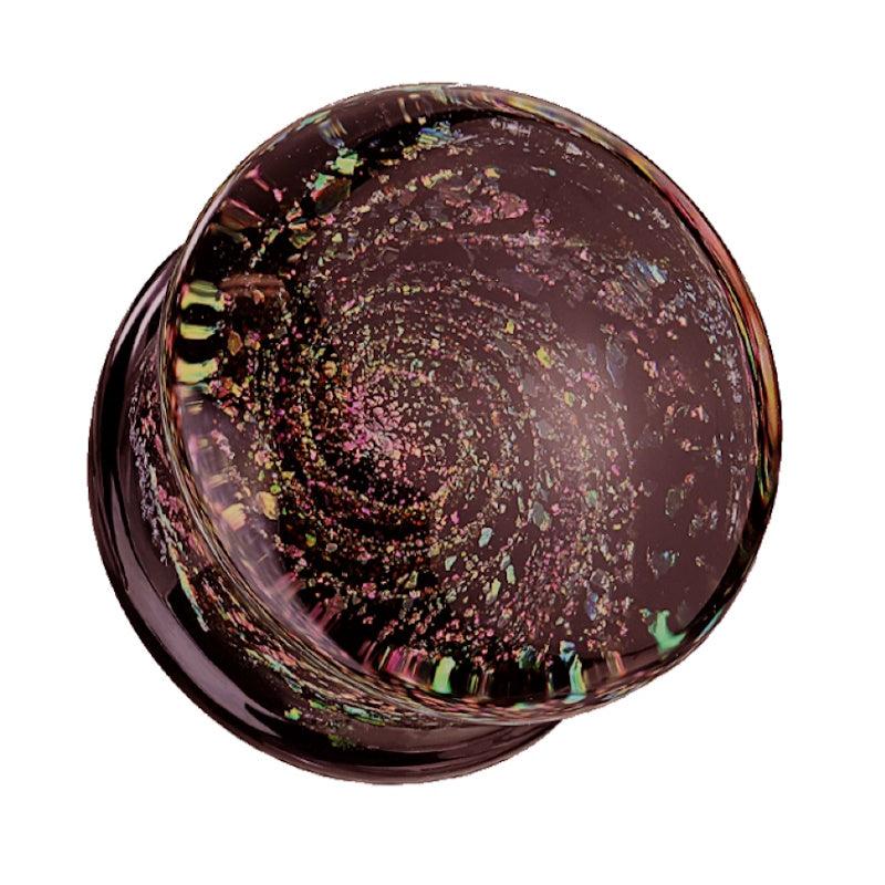 One of a pair of spiral galaxy ear gauges with a glitter spiral galaxy design embedded in the glass pictured against a white background.